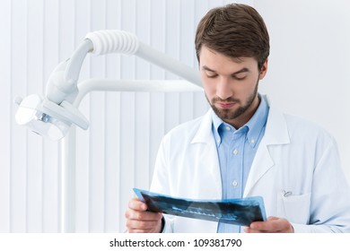 Dentist carefully studies the roentgenogram, whte background