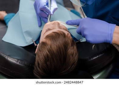 The dentist checks teeth of boy who is sitting in a dental chair. Dental treatment. - Powered by Shutterstock