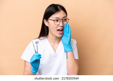 Dentist Chinese Woman Holding Tools Isolated On Beige Background Shouting With Mouth Wide Open To The Side