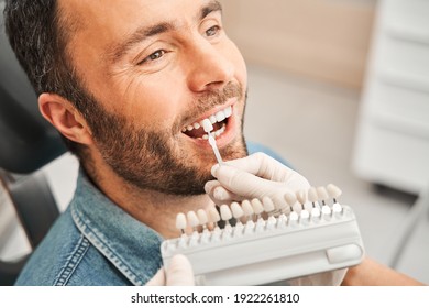 Zahnarzt wählt Farbe der Zahnemaille in der Patientin. Zahnarzt in weißen medizinischen Handschuhen, die Proben aus der Zahnemaille auf die Zähne des Patienten mit leidenschaftlicher Kaukasier auftragen. Stockfoto
