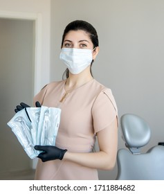 The Dentist In The Clinic Holds A Toothpick In His Hands. Nurse In Respirator With In Dental Office With Tools