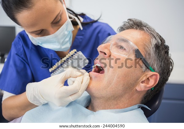 Dentist comparing teeth whitening of her patient\
in dental clinic