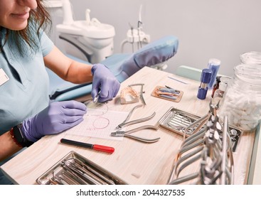 Dentist Cutting Braces Wire While Sitting At The Table With Orthodontic Instruments. Woman Orthodontist Preparing Wire For Braces Attachment. Concept Of Dentistry And Orthodontic Treatment.