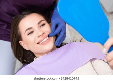 Dentist demonstrates the result of teeth treatment or professional dental cleaning, while happy patient looks in the mirror - Powered by Shutterstock