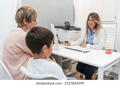 A dentist discusses treatment with a mother and her son during a consultation in a modern clinic. Concept of professional dental care and patient-family interaction. - Powered by Shutterstock