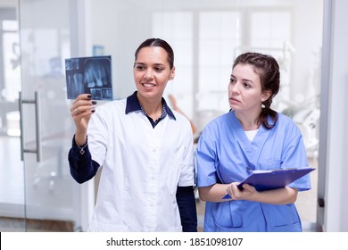 Dentist doctor holding teeth x-ray and nurse taking notes on clipboard in stomatology office. Stomatolog and her assistant in reception of dental clinic looking at teeth radiography.