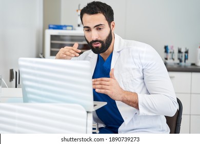 Dentist Doctor Sitting At Desk With Laptop Computer In His Cabinet Or Office And Having Video Calls With Patients. Man Giving Consultations On Online Chats And Teaching People How To Prevent Caries