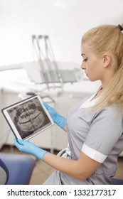 Dentist doctor using digital tablet against dental equipment. Beautiful confident serious woman stomatologist analyzing human teeth x-ray on the digital tablet pc.