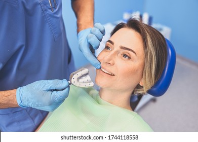 Dentist Examining A Patient's Teeth Using Dental Equipment Impression Spoon In Dentistry Office. Stomatology And Health Care Concept. Doctor In Disposable Medical Facial Mask, Smiling Happy Woman.