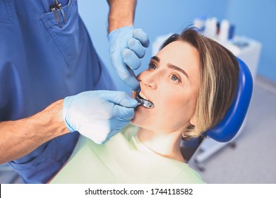 Dentist Examining A Patient's Teeth Using Dental Equipment Impression Spoon In Dentistry Office. Stomatology And Health Care Concept. Doctor In Disposable Medical Facial Mask, Smiling Happy Woman.