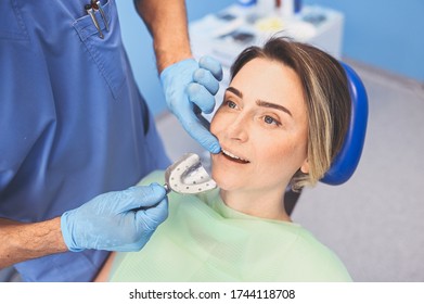 Dentist Examining A Patient's Teeth Using Dental Equipment Impression Spoon In Dentistry Office. Stomatology And Health Care Concept. Doctor In Disposable Medical Facial Mask, Smiling Happy Woman.