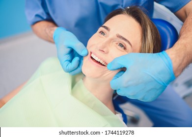 Dentist examining a patient's teeth using dental equipment in dentistry office. Stomatology and health care concept. Young handsome male doctor in disposable medical facial mask, smiling happy woman. - Shutterstock ID 1744119278