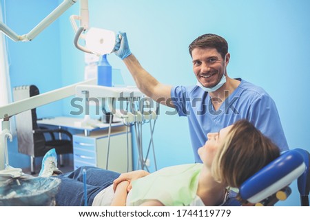 Dentist examining a patient's teeth using dental equipment in dentistry office. Stomatology and health care concept. Young handsome male doctor in disposable medical facial mask, smiling happy woman.