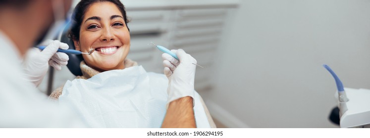 Dentist examining teeth of a female patient in dental clinic using dental tools. Happy woman getting dental treatment.