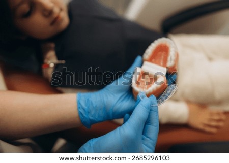 Dentist explaining teeth alignment process using jaw model and invisible braces to young patient in dental clinic