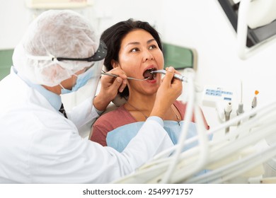 Dentist in face mask treating asian female patient using dental drill in dentist office - Powered by Shutterstock