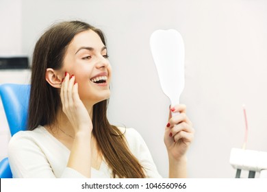 Dentist finishing successful teeth restoration, black haired doctor, in green mask, giving to happy patient mirror, beautiful long-haired woman looking at pristine white teeth with great pleasure