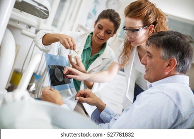 Dentist and her female assistant  in dental office talking with senior  patient and preparing for treatment.Examining x-ray image.