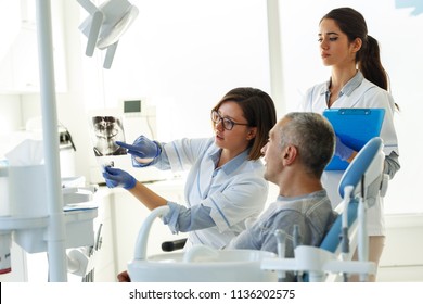 Dentist and his assistant in dental office talking with female patient and preparing for treatment.Examining x-ray image. - Powered by Shutterstock