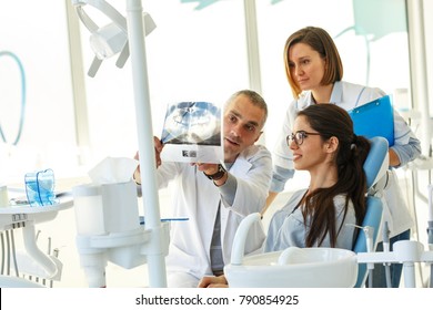 Dentist and his assistant in dental office talking with young female patient and preparing for treatment.Examining x-ray image.