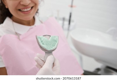 Dentist holding dental impressions on the background of a patient woman smiling toothy smile. Dental molds from upper jaw of silicone material. Imprint of the tooth row of high precision. - Shutterstock ID 2070613187