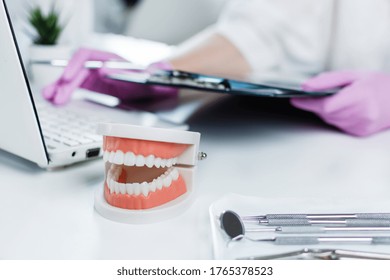 Dentist holding medical exam card of patient and using computer in dentist's clinic. Teeth care and treatment concept. Dental insurance.