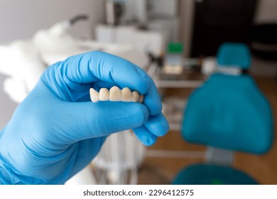 The dentist holds a ceramic, zirconium, bridge-shaped, non-removable dental prosthesis in his hand. Dental bridge. - Shutterstock ID 2296412575