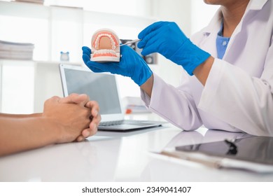 The dentist holds a denture in his hand and shows the patient the position of the problem tooth and the dentist explains how to treat the tooth for the patient to understand. Copy space for text