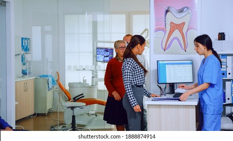 Dentist Inviting Senior Man In Consultation Dental Room While Nurse Giving To Patient Form To Fill Indicating To Sit On Chair In Waiting Area. Slow Motion Shot Crowded Professional Orthodontist Office