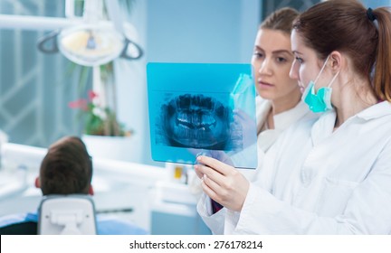 Dentist looking at roentgen of human jaw. Consulting. Patient blurred on chair in background. - Shutterstock ID 276178214