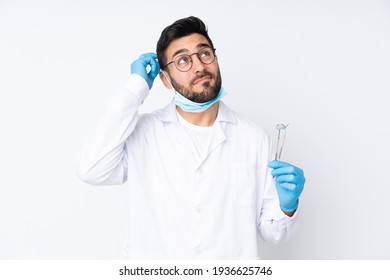 Dentist man holding tools isolated on white background having doubts and with confuse face expression