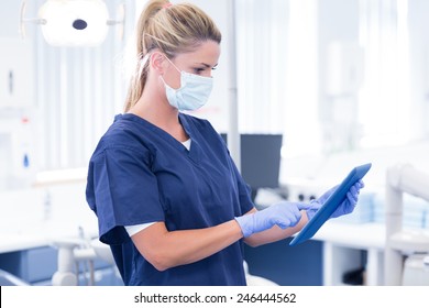 Dentist In Mask And Blue Scrubs Using Her Tablet At The Dental Clinic