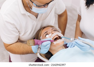 A Dentist In A Mask And Goggles Treats A Woman's Teeth.