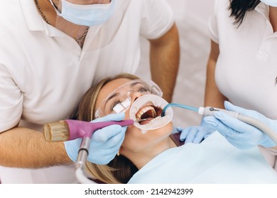 A Dentist In A Mask And Goggles Treats A Woman's Teeth.