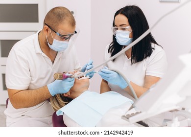 A Dentist In A Mask And Goggles Treats A Woman's Teeth.