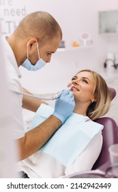 A Dentist In A Mask And Goggles Treats A Woman's Teeth.