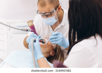 A Dentist In A Mask And Goggles Treats A Woman's Teeth.