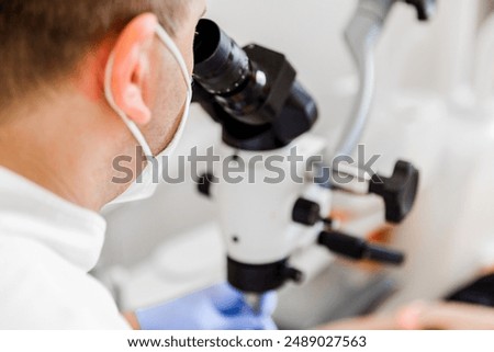 Dentist in mask using a microscope to examine a patient's teeth during a procedure in a modern dental clinic.