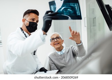 The dentist observes a x-ray image of his patient. Dentist is wearing protective face mask and shield due to coronavirus pandemic.	