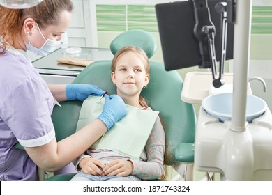 Dentist On Protective Mask And Child With Screen In Stomatology Office. Young Girl With On The First Dental Visit