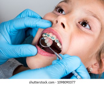 Dentist, Orthodontist examining a little girl patient's teeth carrying braces