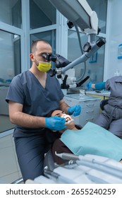 Dentist Performing a Procedure Under Microscope in Modern Dental Office with Patient Relaxed for Treatment and Assistant on Background Preparing Tools