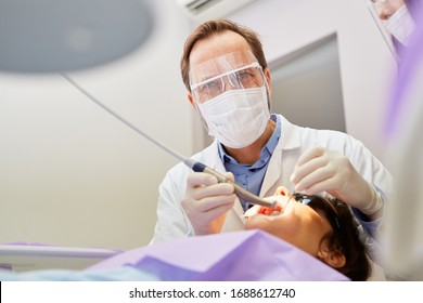 Dentist With Protective Mask And Drill While Treating Patient In The Dental Office