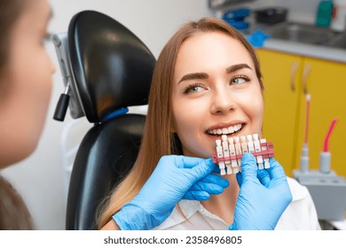 Dentist selects a shade of teeth whitening using shade guide to young patient with perfect smile.
