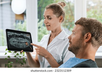 dentist showing and explaining dental x-ray picture with impacted wisdom tooth to his patient - Shutterstock ID 2323112309