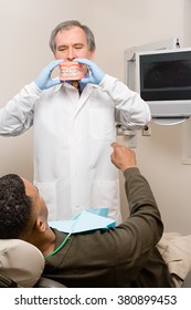 Dentist showing patient false teeth - Shutterstock ID 380899453