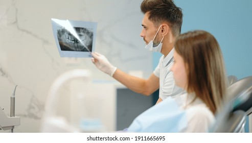 Dentist showing x-ray of a jaw for a young patient during an orthodontic treatment. Girl having a consultation with an orthodontist. 4k video screenshot, please use in small size