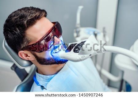 Dentist starting teeth whitening procedure with young man.