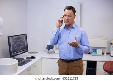Dentist Talking On Mobile Phone At Dental Clinic