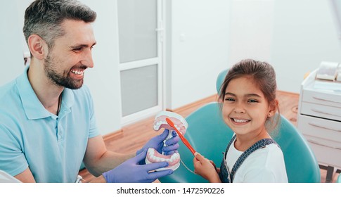 Dentist Teaching Little Mixed Race Girl Brushing Teeth Using Human Teeth Model At Dental Clinic